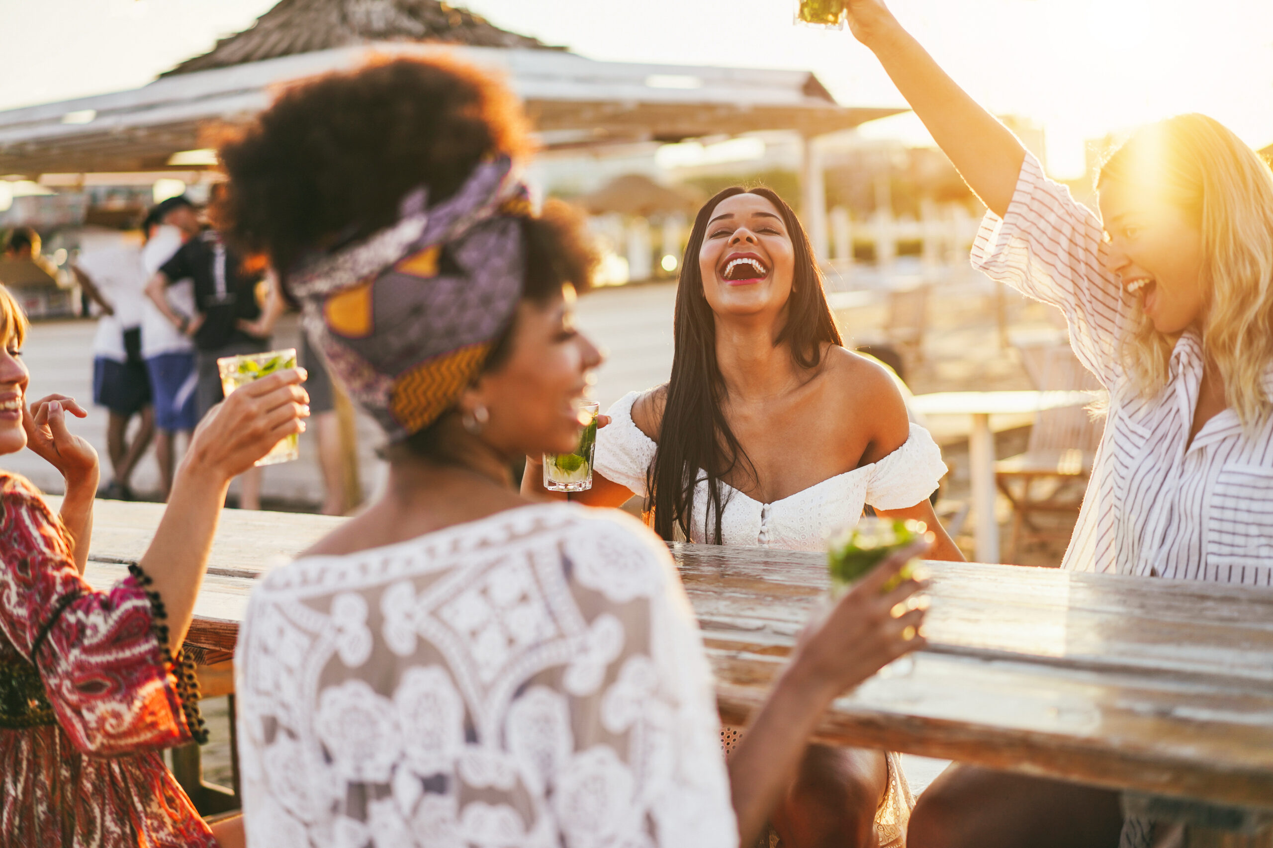 Happy girls having fun drinking cocktails at bar on the beach - Focus on african girl face